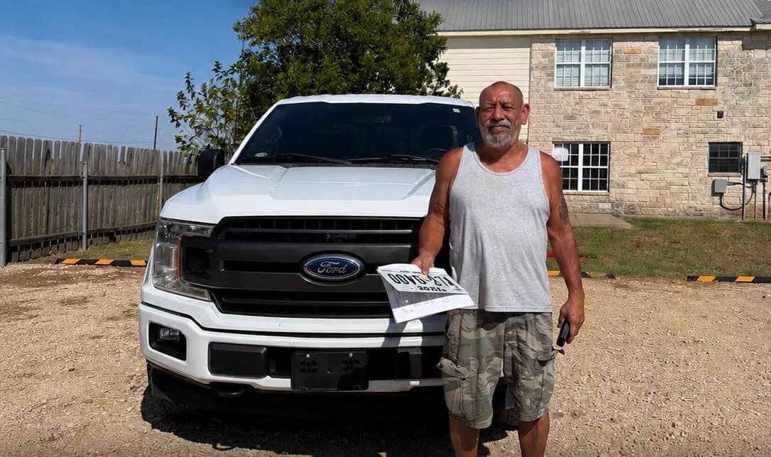 A customer standing beside the white Ford F-150 he bought, holding the paperwork, on the lot in Hutto.