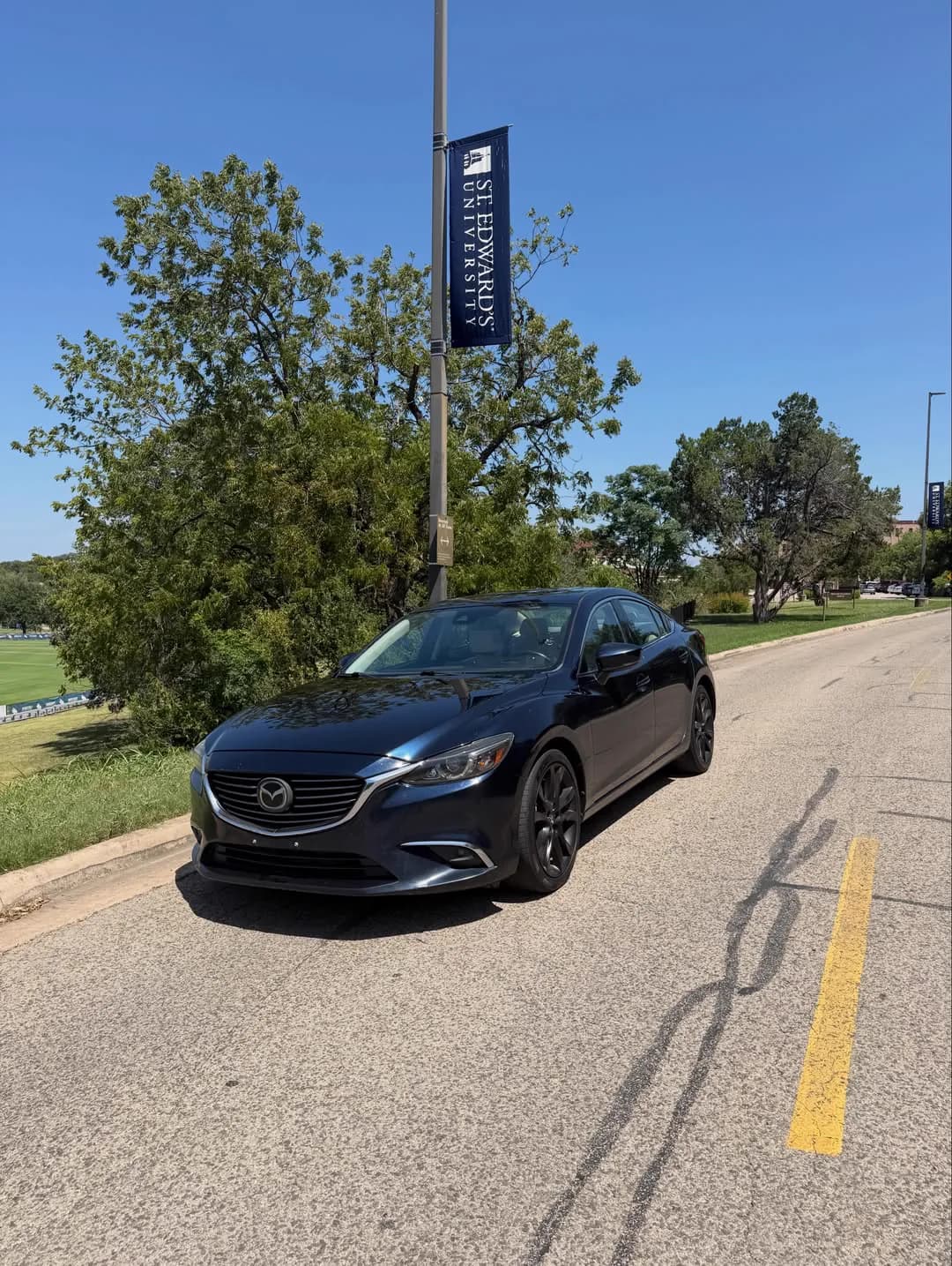 The dark blue Mazda 6 photographed from the front three-quarter on a quiet street.